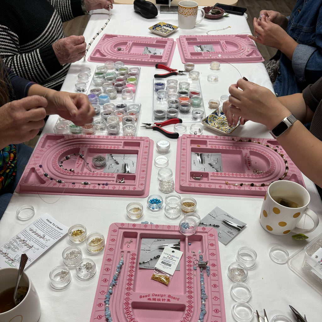 People working on jewelry-making projects with pink trays and tools on a table.